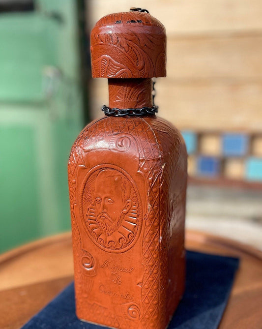 A vintage leather bound decanter with embossed imagery of Don Quixote author Miguel de Cervantes and Spanish text 27cm tall